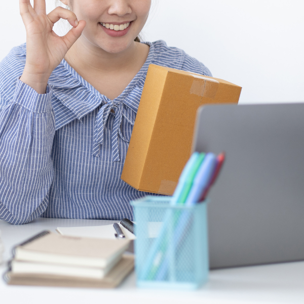 a woman holding a package while talking to someone via laptop